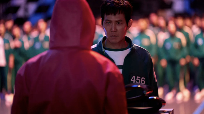 Lee Jung-jae as Seong Gi-hun ​​standing before a Squid Game worker about to vote