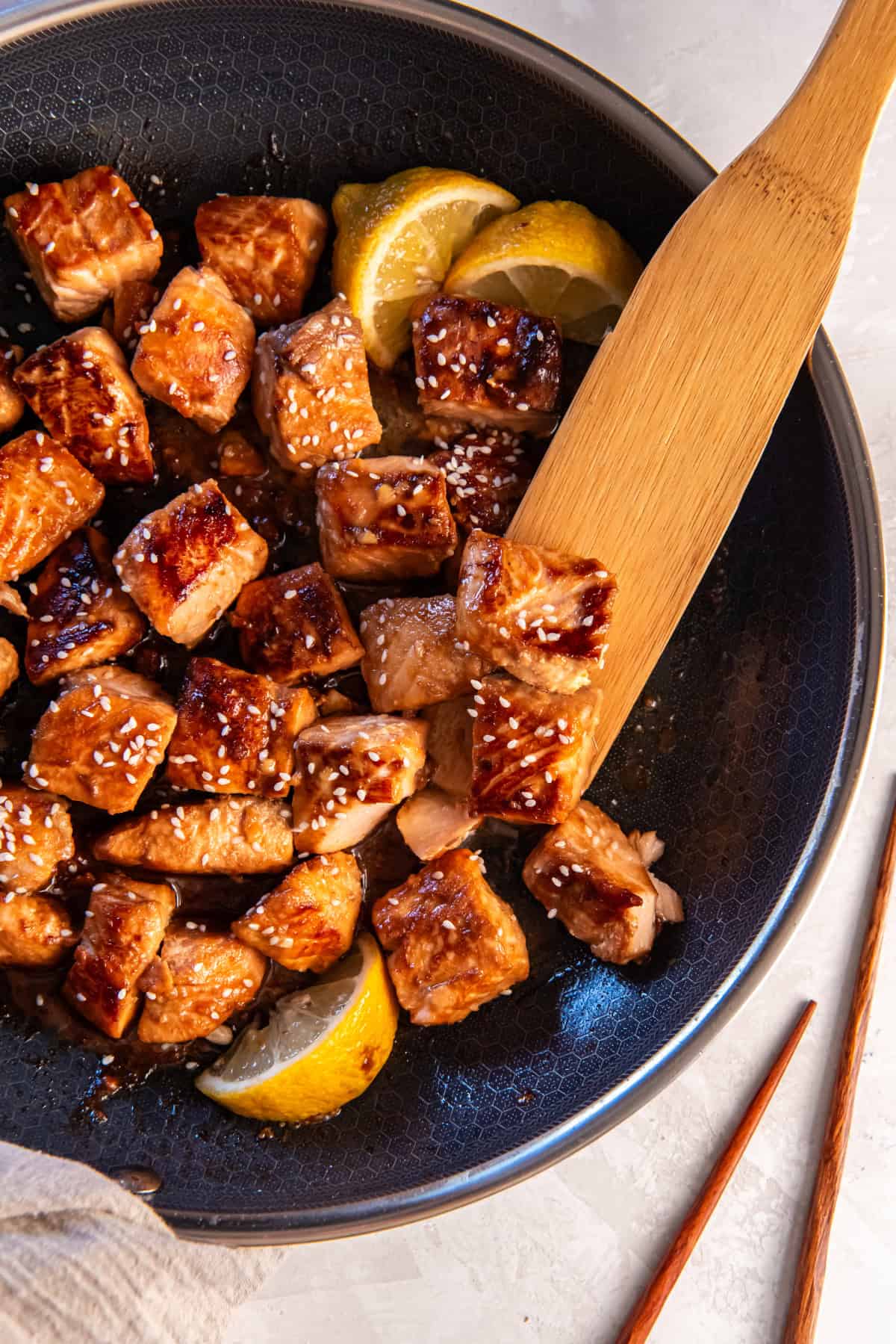 Up close picture of honey garlic salmon bites in pan with a wood spatula.