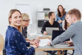 Frau sitzt mit anderen am Tisch, mit Laptops