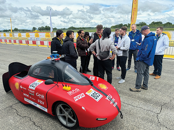 A red vehicle with a group of team members standing behind it, getting ready for the challenges.