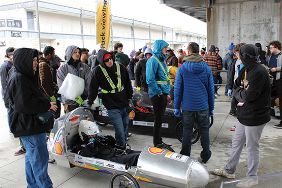 A group of people stand over a speedway car waiting for the competition to start.