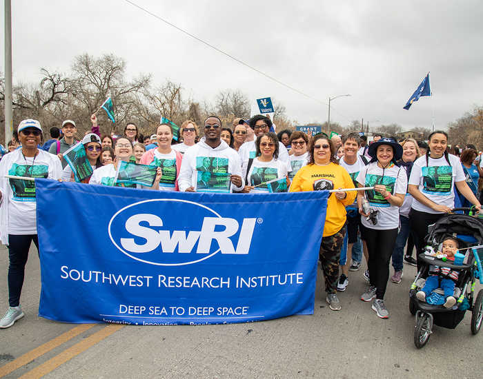 SwRI employees wearing MLK shirts standing behind a blue Southwest Research Institute banner 