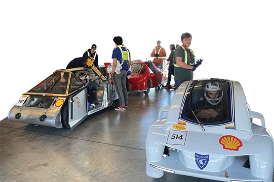 Two teams standing and looking over their respective prototype vehicle made for competition. 