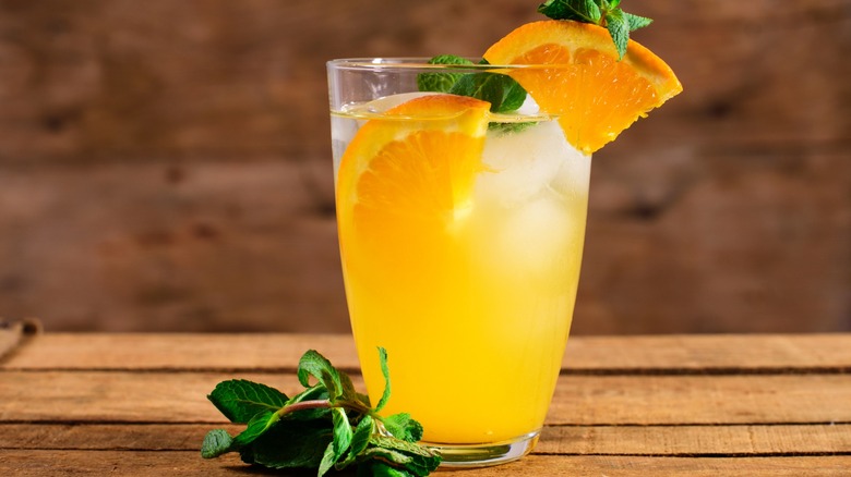 An orange mocktail garnished with mint and oranges