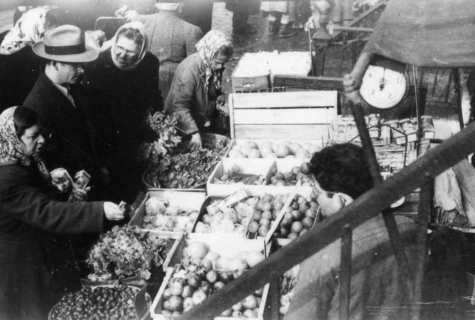 Close-up photo of pushcarts with crates full of fresh fruits and vegetables. Some customers are looking and picking produce.