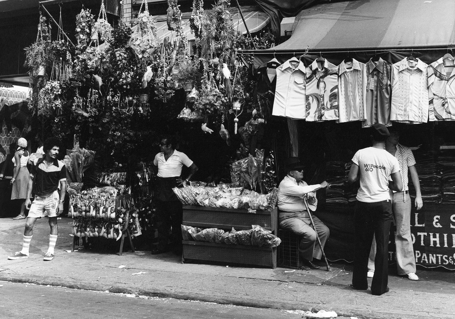 Old shops on Orchard Street almost overflowing with t-shirts and plants hanging on display as the owners stand out front with costumers