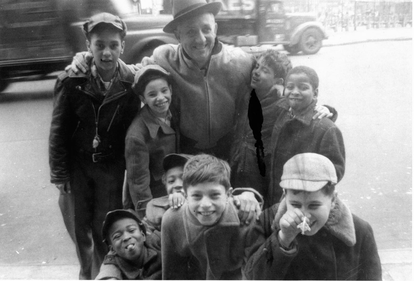 Group photo of an older adult with light skin tone and 8 children of varying skin tones gathered around, all smiling and laughing