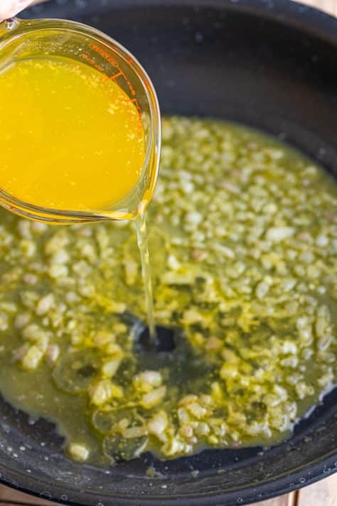 Chicken broth being added to the shallot mixture in a skillet.