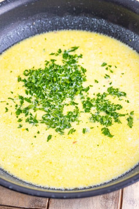 Parsley and lemon juice added to cream sauce in a pan.