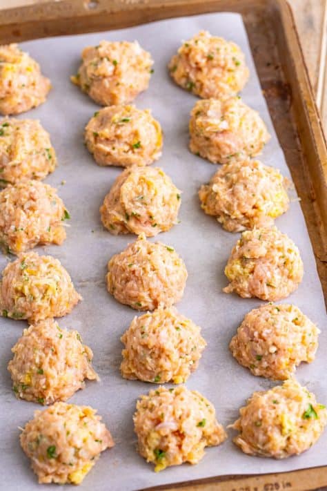 Raw meatballs on a lined baking sheet.