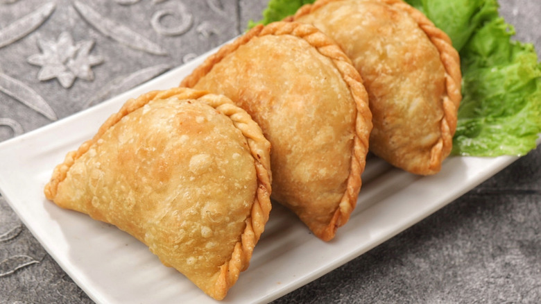 Empanadas on a white plate with lettuce on a gray, patterned background