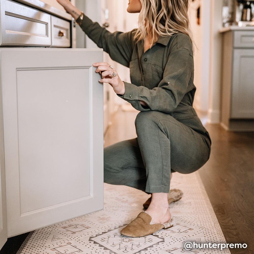 Neutral boho print kitchen mat shown in kitchen with woman bending down to open a cabinet.