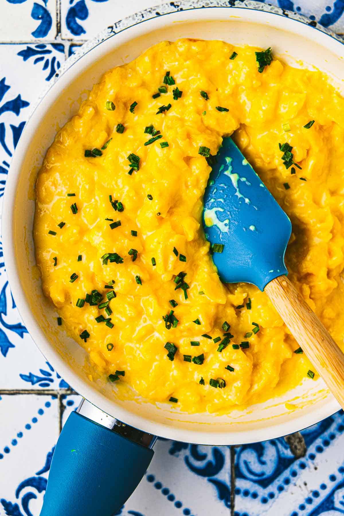 soft scrambled eggs topped with chives being stirred with a spatula in a saucepan.