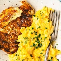 soft scrambled eggs topped with chives next to toast on a plate with a fork.