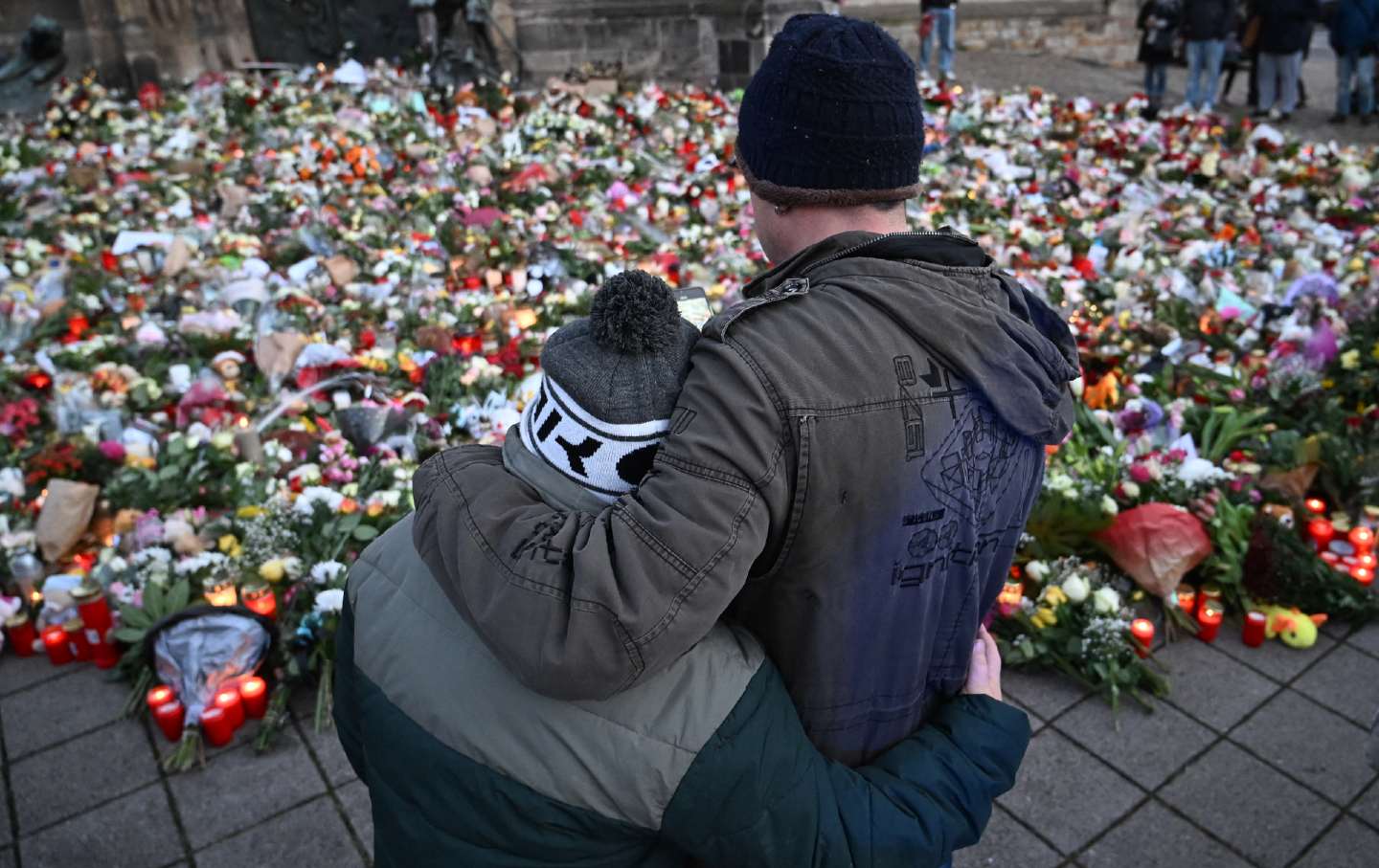 Mourners hug in front of a makeshift memorial of flowers and candles for the victims of a car-ramming attack on a Christmas market in Magdeburg, eastern Germany, on December 23, 2024.