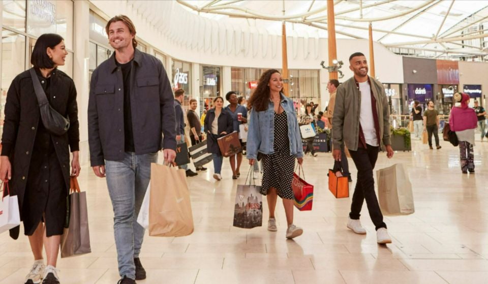 Two couples carry shopping bags walking through a light bright shopping mall 