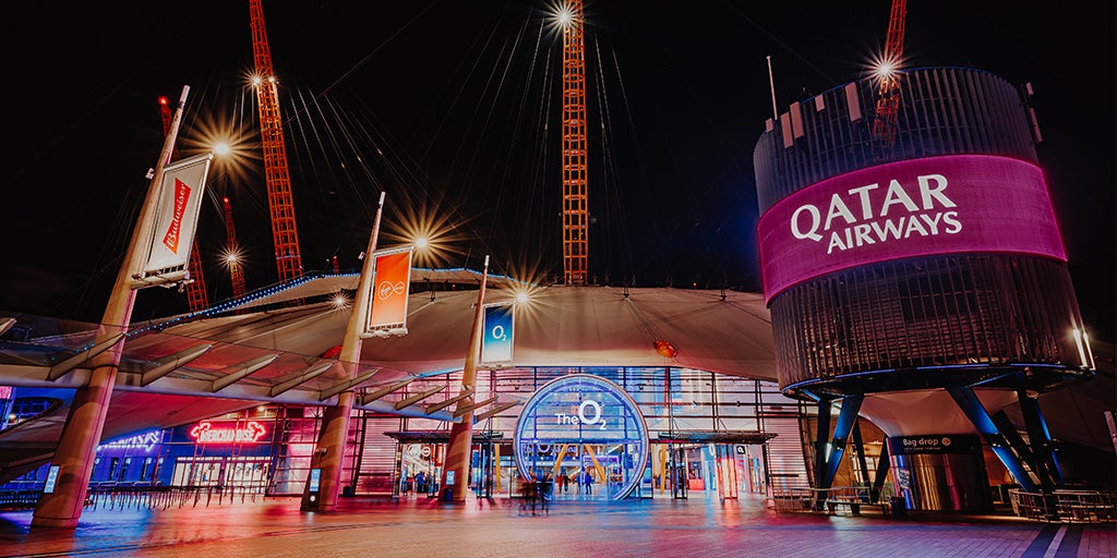 Image of the front entrance of The O2 with Qatar Airways logo on a burgandy background on a large cylnder outside The O2 