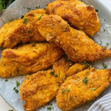 crispy oven fried chicken on a plate lined with parchment paper.