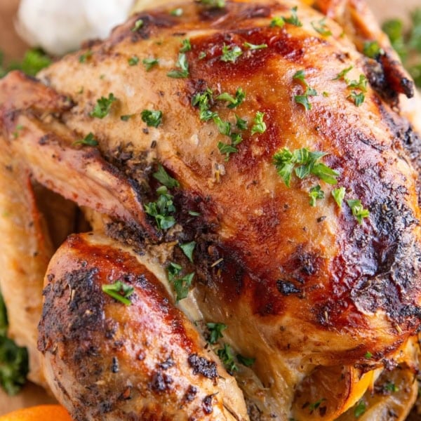 Whole roast turkey on a wooden cutting board with sliced oranges and fresh garlic in the background.