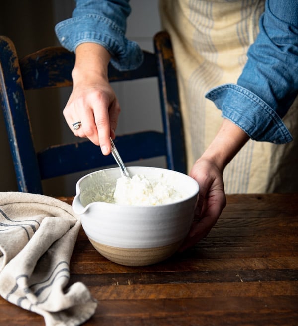 Stirring together sour cream and cream cheese mixture in a white bowl.