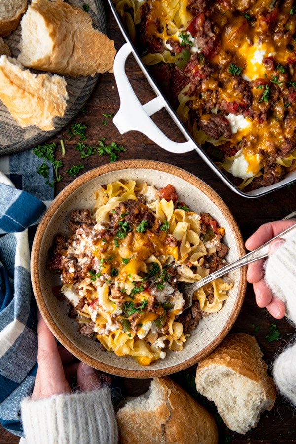 Overhead image of hands eating a bowl of sour cream noodle bake.