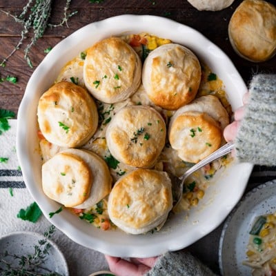 Square overhead shot of hands serving a chicken pot pie recipe with biscuits