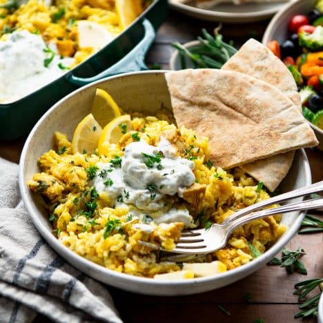 Square side shot of a bowl of chicken tzatziki with rice and fresh herbs on a dinner table.