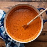 Overhead shot of a Dutch oven full of creamy beef tomato soup on a wooden table.