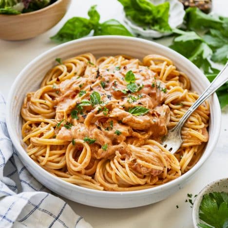 Square side shot of a white pasta bowl full of crock pot cream cheese chicken with spaghetti.