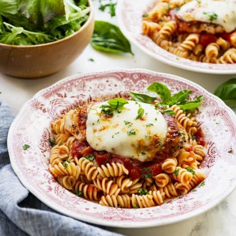 Square side shot of a plate of healthy chicken parmesan on a bed of pasta with marinara.