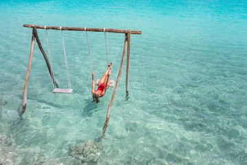 View of woman swinging on white sand beach relaxing and sunbathing by the lagoon in Mexico