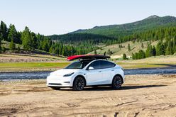 A Tesla Model Y by a river with a stand up paddle board on the roof