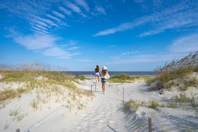 Women walking on pathway through sand dunes leading to the ocean on Jekyll Island, Georgia