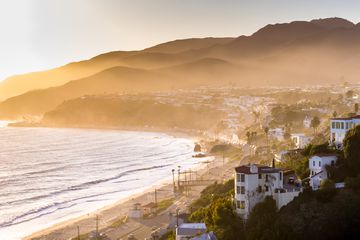 Aerial panorama of the Pacific Coast Highway hugging the beach and curving between the ocean and the town of Malibu, California.