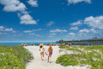 Teenage girls relaxing on the beautiful beach, People enjoying summer vacation by the ocean.Girls walking on the beach. Cloudy sky and pier in the background. Folly Beach, South Carolina USA.