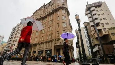 Imagem mostra pessoas andando no Centro de Curitiba com guarda chuva.