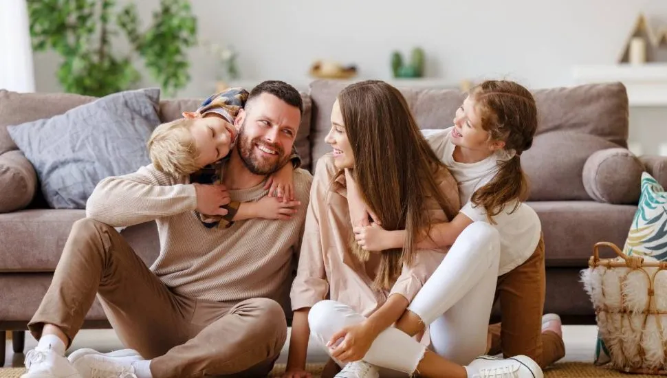 Imagem mostra uma familia sentada no chão com as crianças brincando e os pais se olhando.