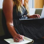 person writing on a notebook beside macbook