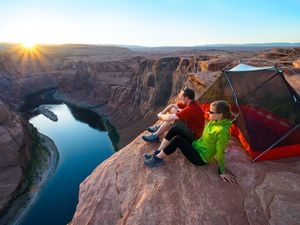 A man and a woman sit outside a tent on the edge of the Grand Canyon