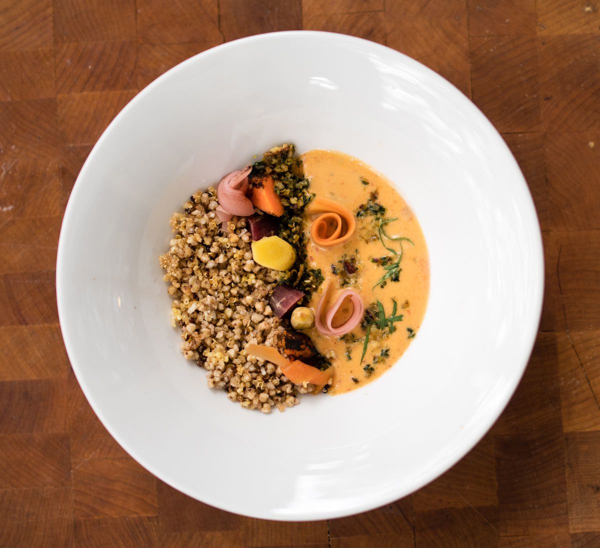 orange sauce and a grain in a white bowl garnished with carrot shaving