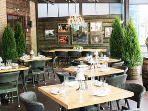 brightly lit room in a restairant with 6 set tables in view. The room is decorated with barrels and potted plants