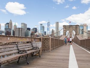 People walking down the brooklyn bridge with the manhattan skyline behind them