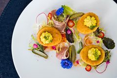 3 Deep fried deviled eggs garnished with flowers and greens, and charcuterie on a white plate