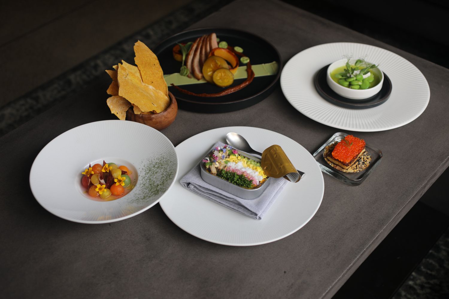 Full spres at Verita restaurant with lima beans in a bowl on one plate, a opened sardine tin with finely diced vegetables on a second plate, slice pork on a fourth, melon-balled fruit on a fourth, a small sqaure plate with caviar and crackers and a bowl with chips