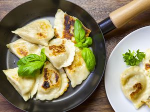 pan-fried pierogi dumplings in a frying pan on a table with a plate of pierogis beside