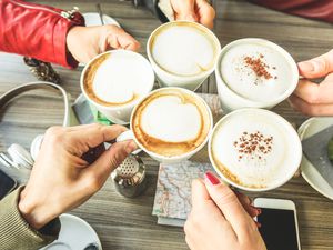 Cropped Hands Of People Toasting Coffee Over Table At Restaurant