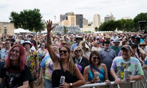 A large outdoor festival audience with downtown St. Paul in the background.
