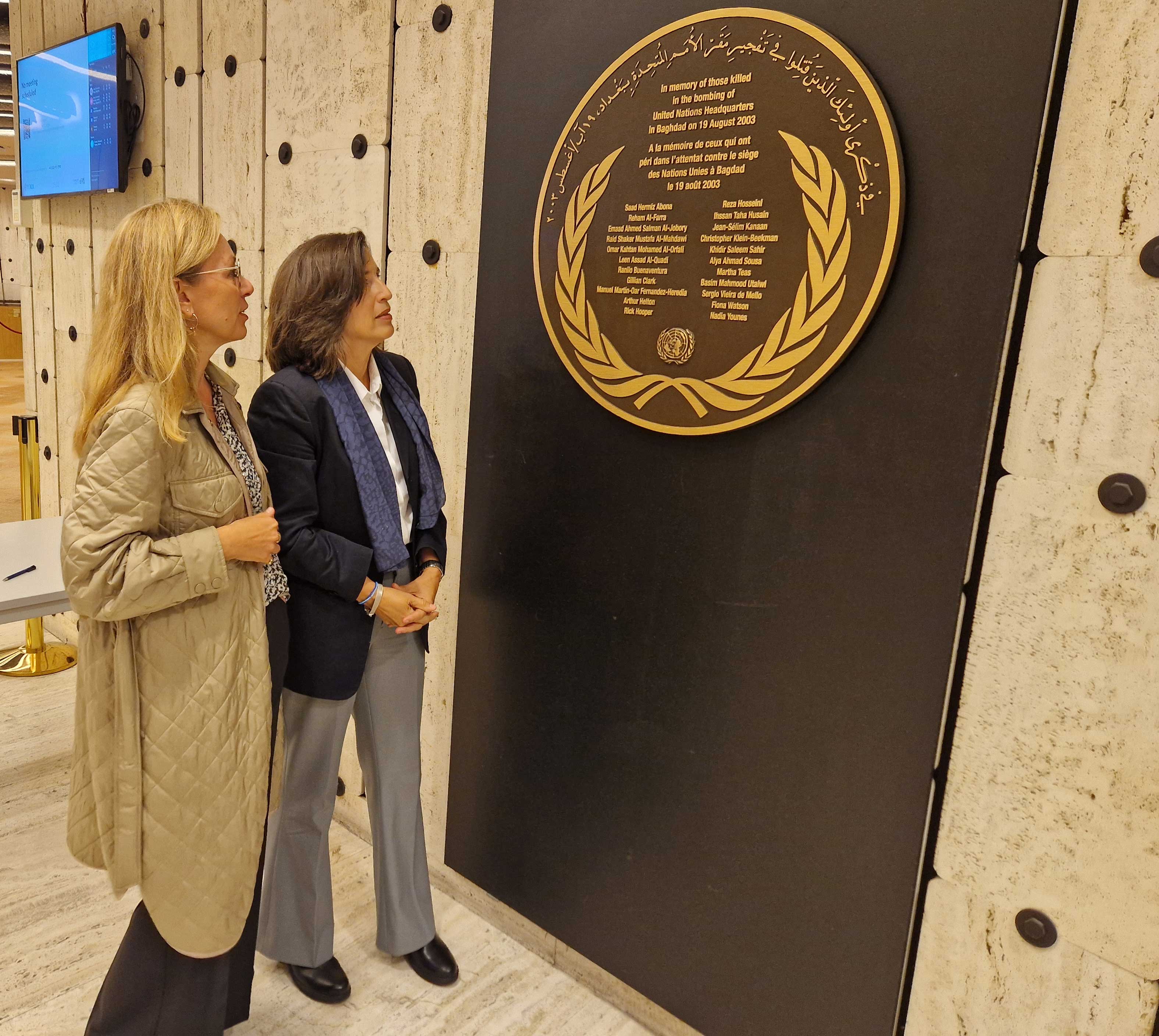 Laura and Melissa look at a commemorative plaque that is hanging on a wall next to them