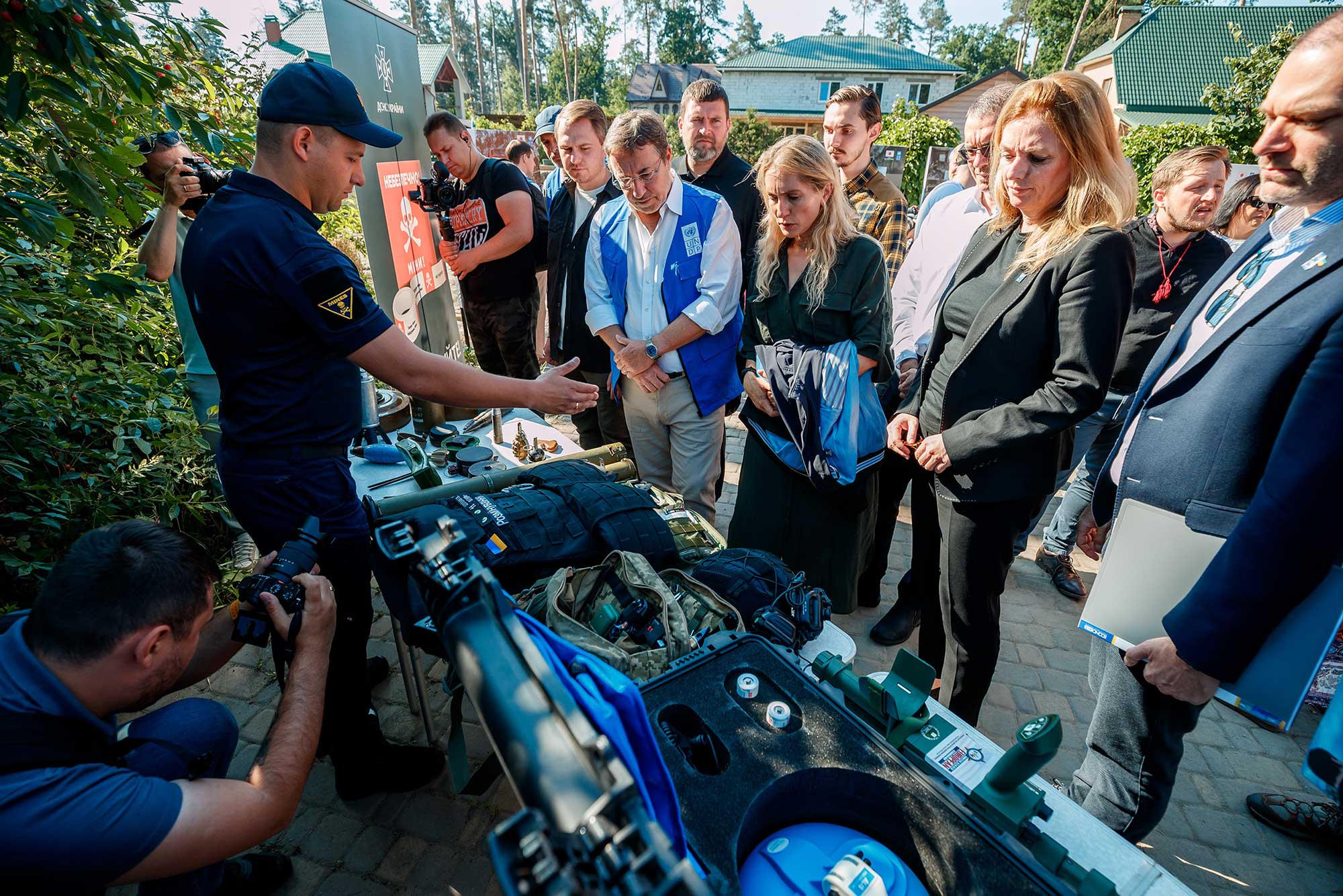 Achim, with a group of people, inspects a table carrying various types of deadly explosive ordnance