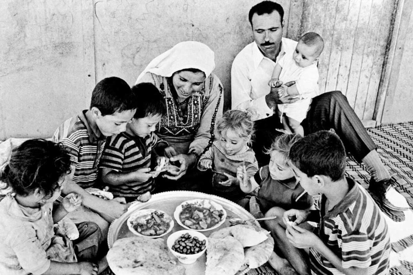 a Palestinian family of nine eating a simple meal of bread, olives and two small dishes together on the floor